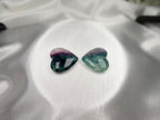 Treasured Energies polished fluorite crystal hearts in purple and green hues resting on a white satin fabric background.