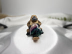 Treasured Energies polished heart-shaped fluorite crystal held by a small platypus figurine on a white satin background.