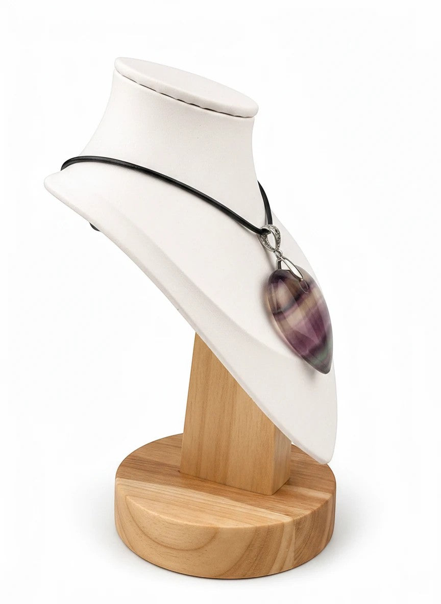 Treasured Energies heart-shaped purple and green fluorite crystal pendant on a black cord necklace displayed on a stand.