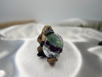 Treasured Energies fluorite crystal worry stone with purple and green bands held by a small platypus figurine on white silk.