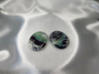 Two smooth, oval-shaped Treasured Energies fluorite crystal worry stones with purple and green banding on a satin fabric.