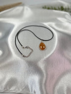 Treasured Energies golden healer quartz teardrop pendant on a black cord necklace resting on white satin fabric.