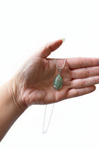 Treasured Energies green aventurine crystal pendant necklace held in a hand, featuring a silver wire-wrapped design.