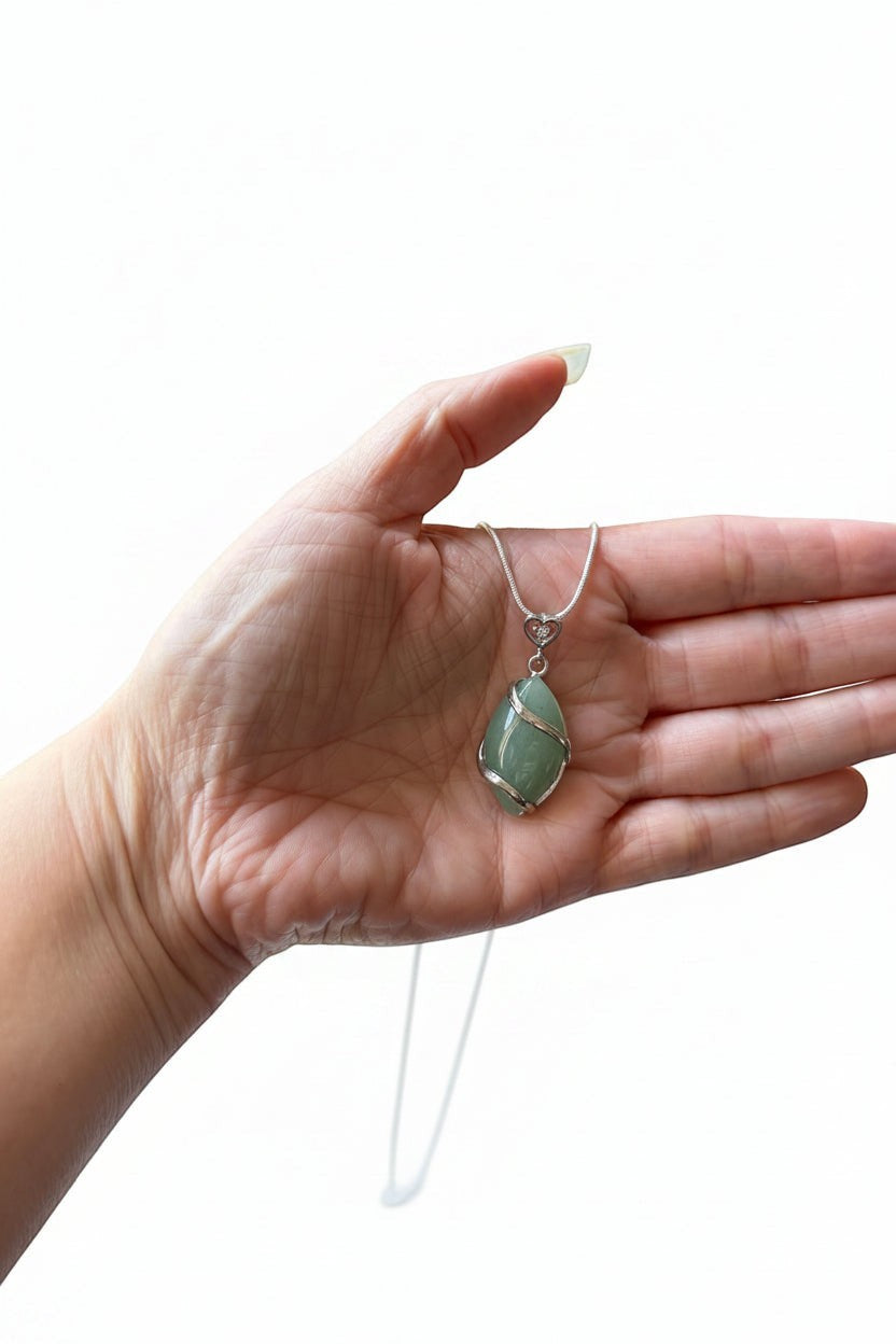 Treasured Energies green aventurine crystal pendant necklace held in a hand, featuring a silver wire-wrapped design.