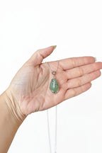 Treasured Energies green aventurine crystal pendant necklace held in a palm, featuring a silver wire-wrapped design.