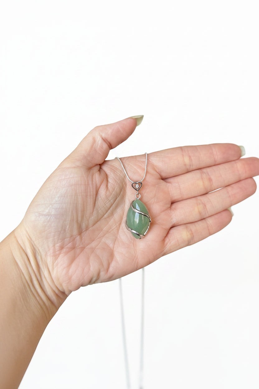 Treasured Energies green aventurine crystal pendant necklace held in a palm, featuring a silver wire-wrapped design.