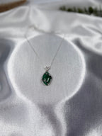 Treasured Energies green aventurine crystal pendant necklace with a silver swirl setting on a white satin background