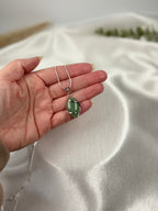 Treasured Energies green aventurine crystal pendant necklace held in a hand against a soft white satin background.