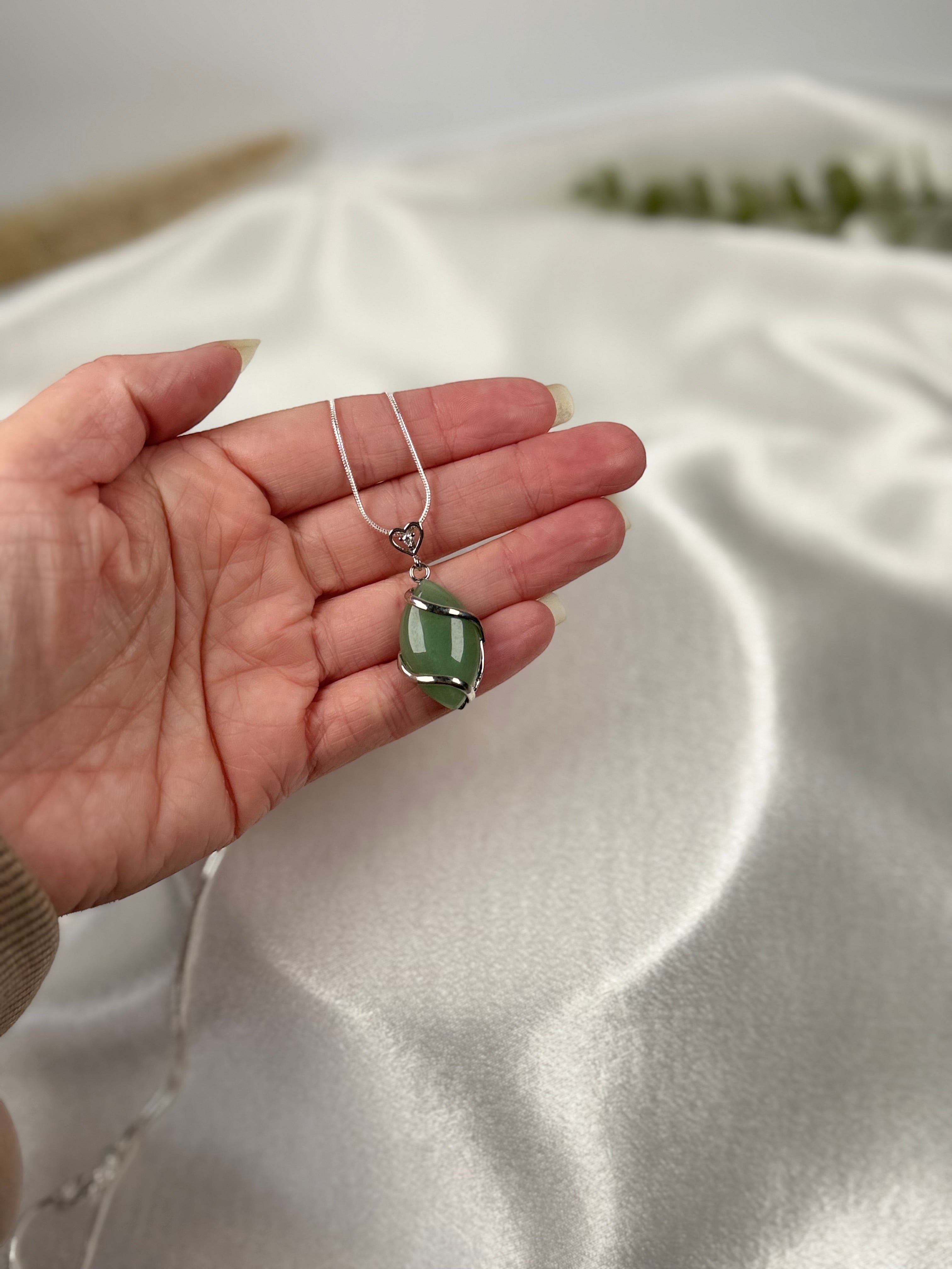 Treasured Energies green aventurine crystal pendant necklace held in a hand against a soft white satin background.