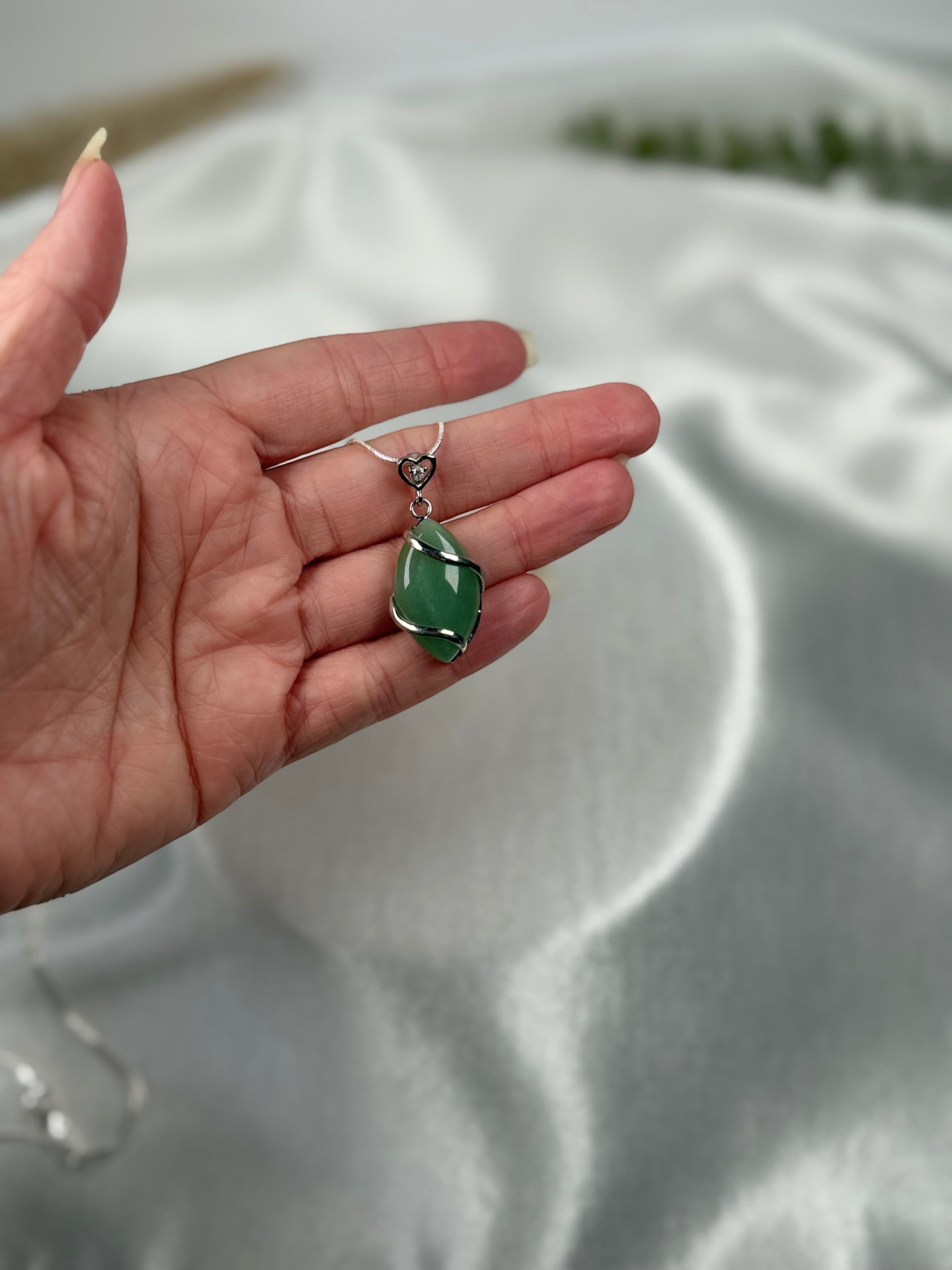 Treasured Energies green aventurine crystal pendant necklace held in a hand against a white satin background
