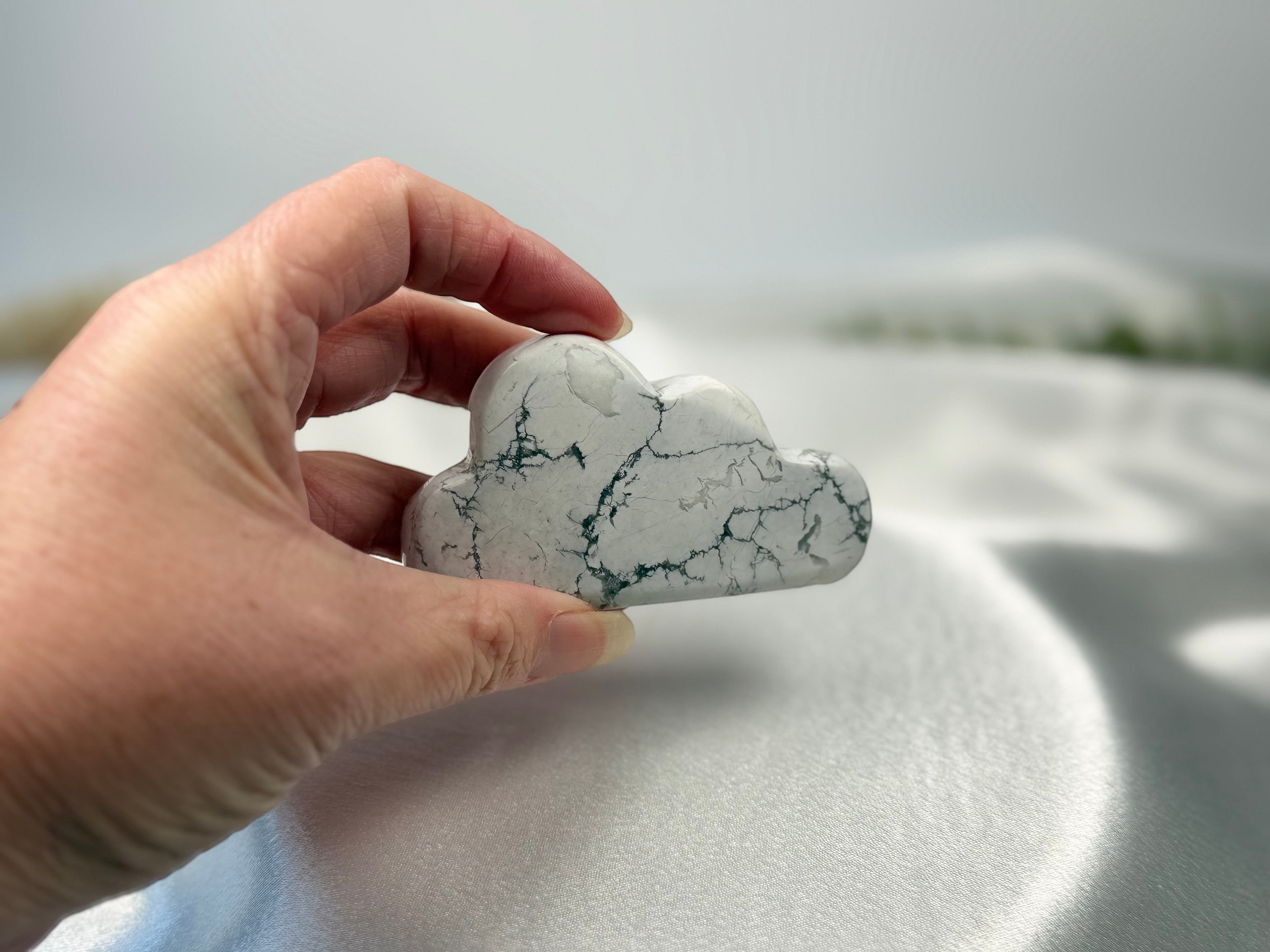 Treasured Energies hand carved howlite crystal cloud with grey web-like veins held in a hand against satin fabric.