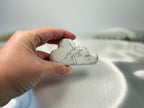 Treasured Energies hand carved howlite crystal cloud with grey veining held in a hand against a white satin background.