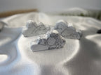 Treasured Energies hand carved white howlite crystal clouds with grey veining on a soft white satin fabric background.