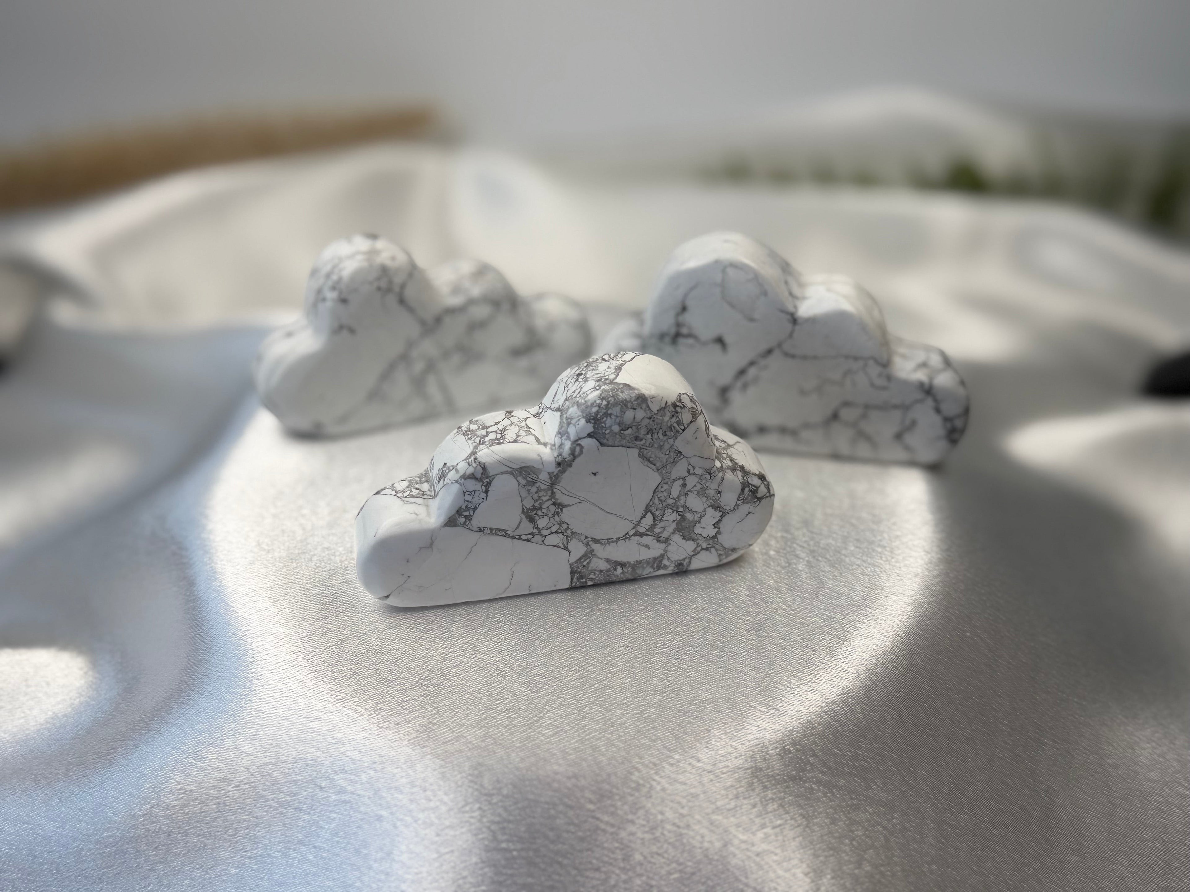 Treasured Energies hand carved white howlite crystal clouds with grey veining on a soft white satin fabric background.
