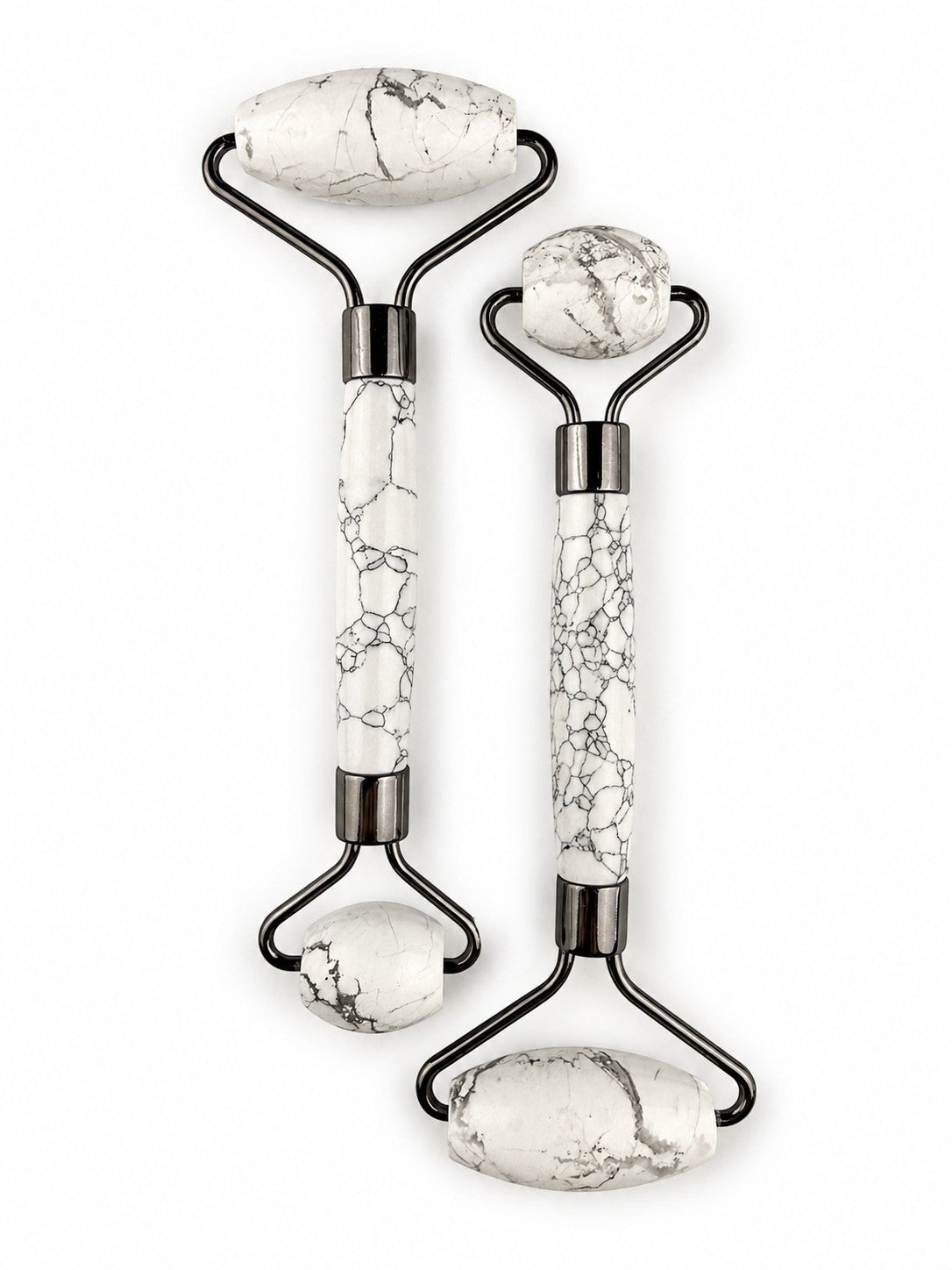 Treasured Energies dual-ended facial massage rollers in white Howlite stone with black veining and dark metal hardware.