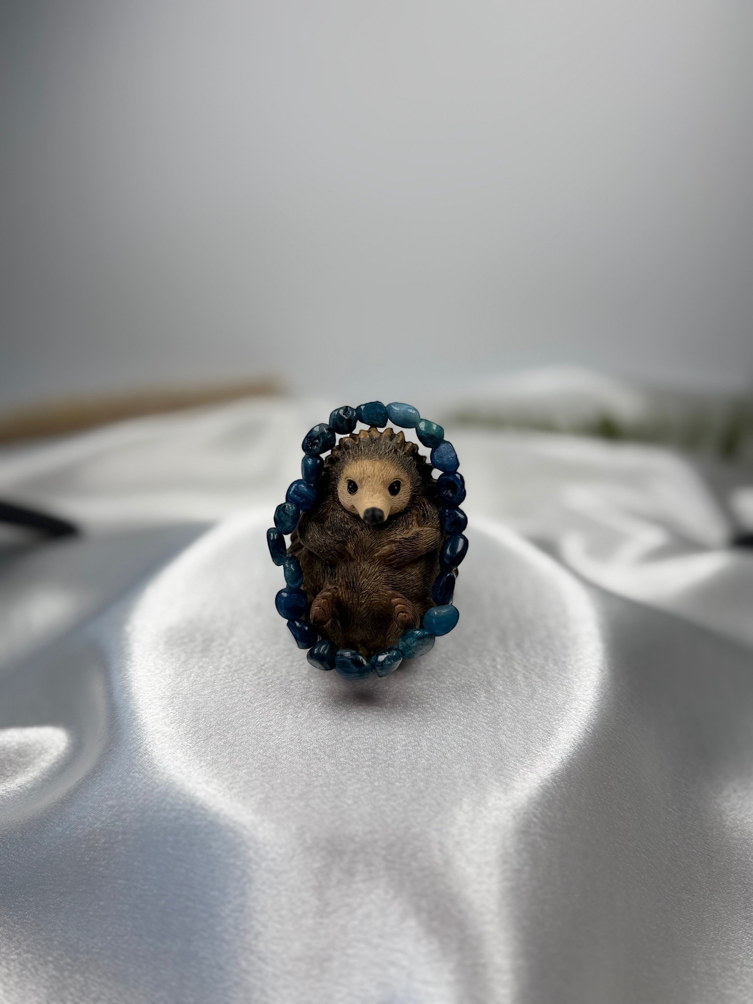 Treasured Energies polished blue kyanite gemstone bead stretch bracelet encircling a small decorative hedgehog figure