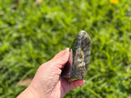 Treasured Energies large polished Labradorite freeform crystal held in hand against a blurred green grass background.
