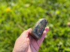 Treasured Energies hand-polished labradorite freeform crystal held in a palm against a blurred green garden background.
