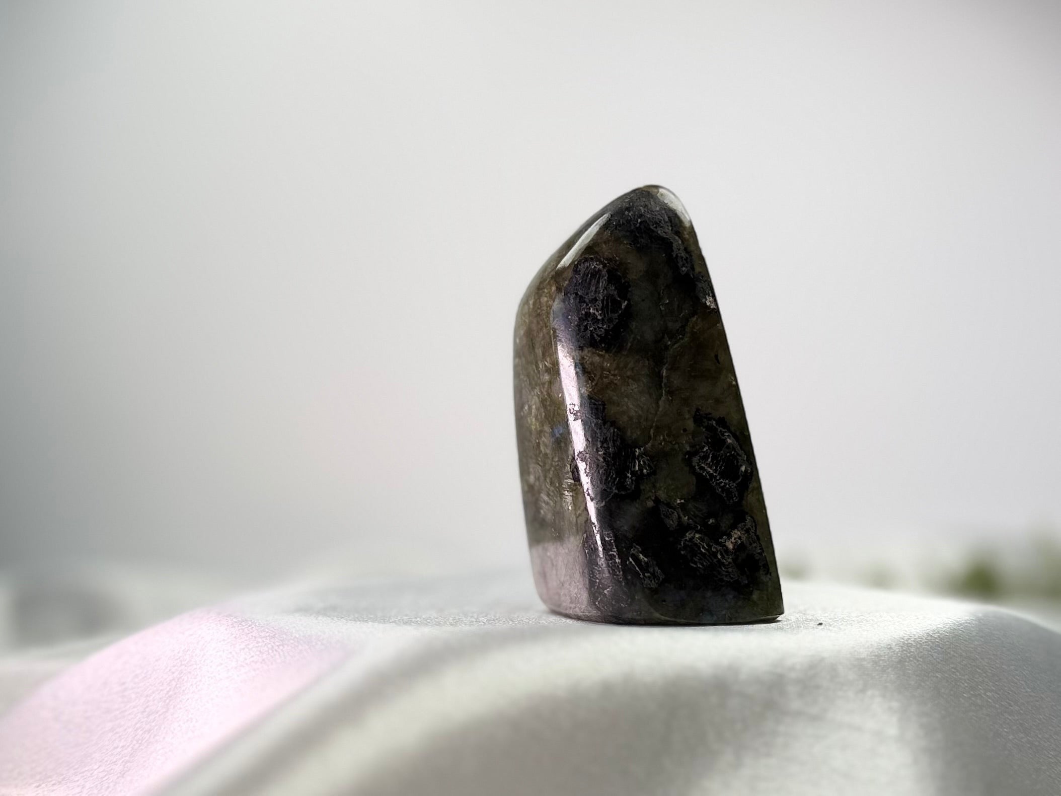 Treasured Energies polished Labradorite freeform crystal with dark grey and iridescent mineral patterns on a white cloth.