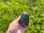 Treasured Energies hand-polished labradorite freeform crystal held against a blurred green outdoor background