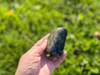 Treasured Energies polished labradorite freeform crystal held in a hand against a blurred green outdoor background