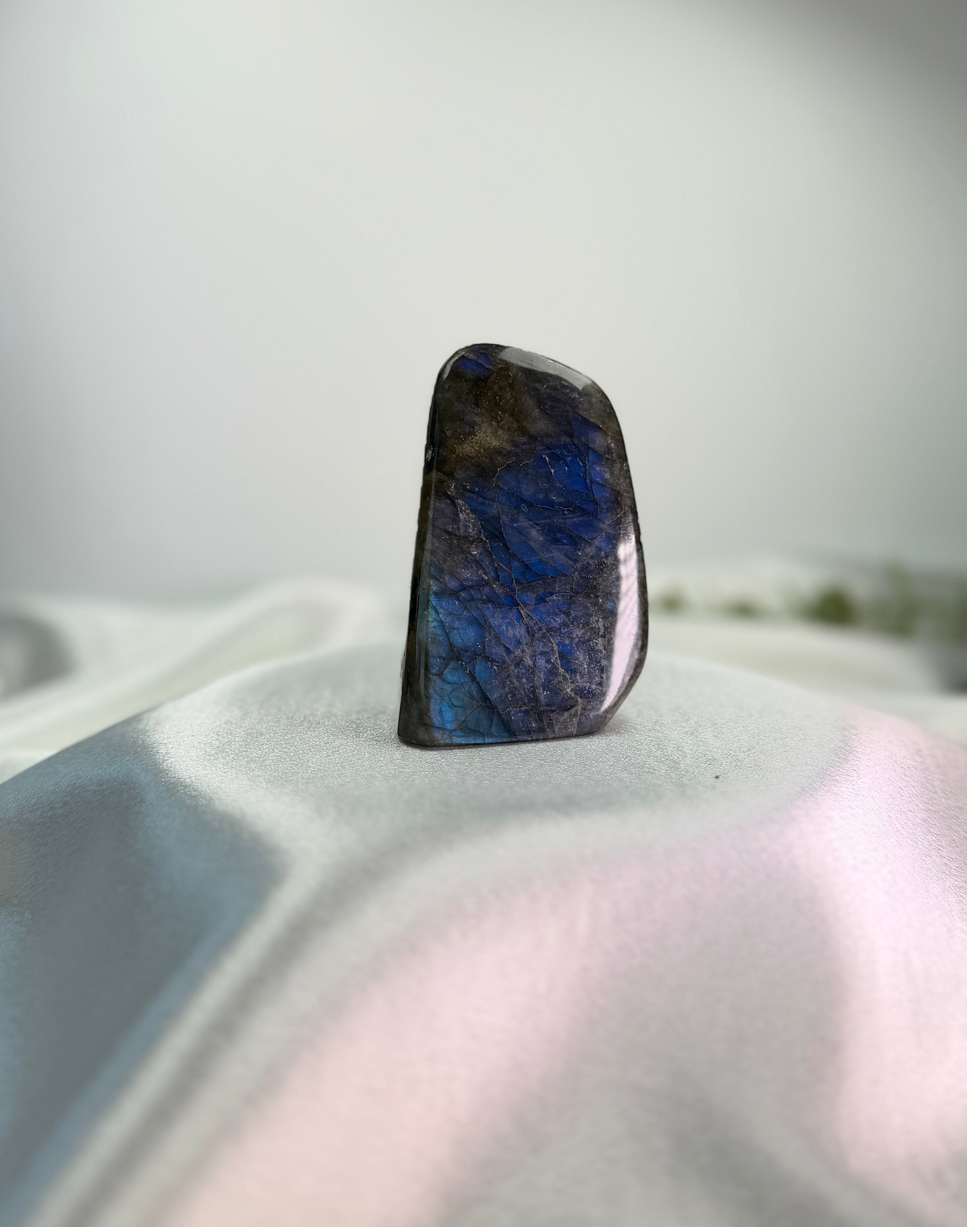 Treasured Energies polished labradorite freeform crystal with vibrant blue labradorescence on a white silk base
