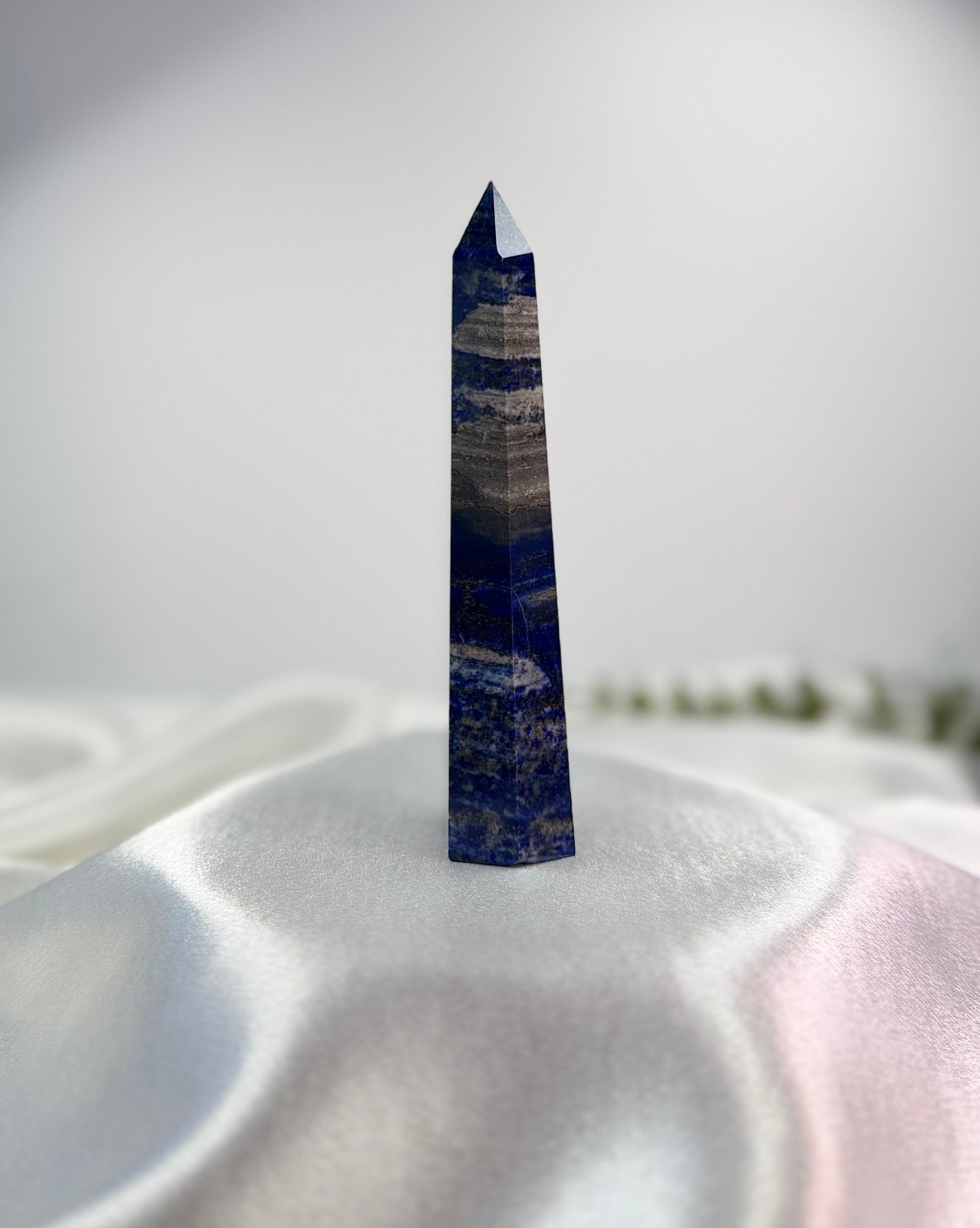 Treasured Energies Lapis Lazuli crystal tower with deep blue tones and natural banding on a white satin background.