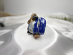 Treasured Energies polished Lapis Lazuli heart crystal held by a small wooden platypus figurine on white satin fabric.