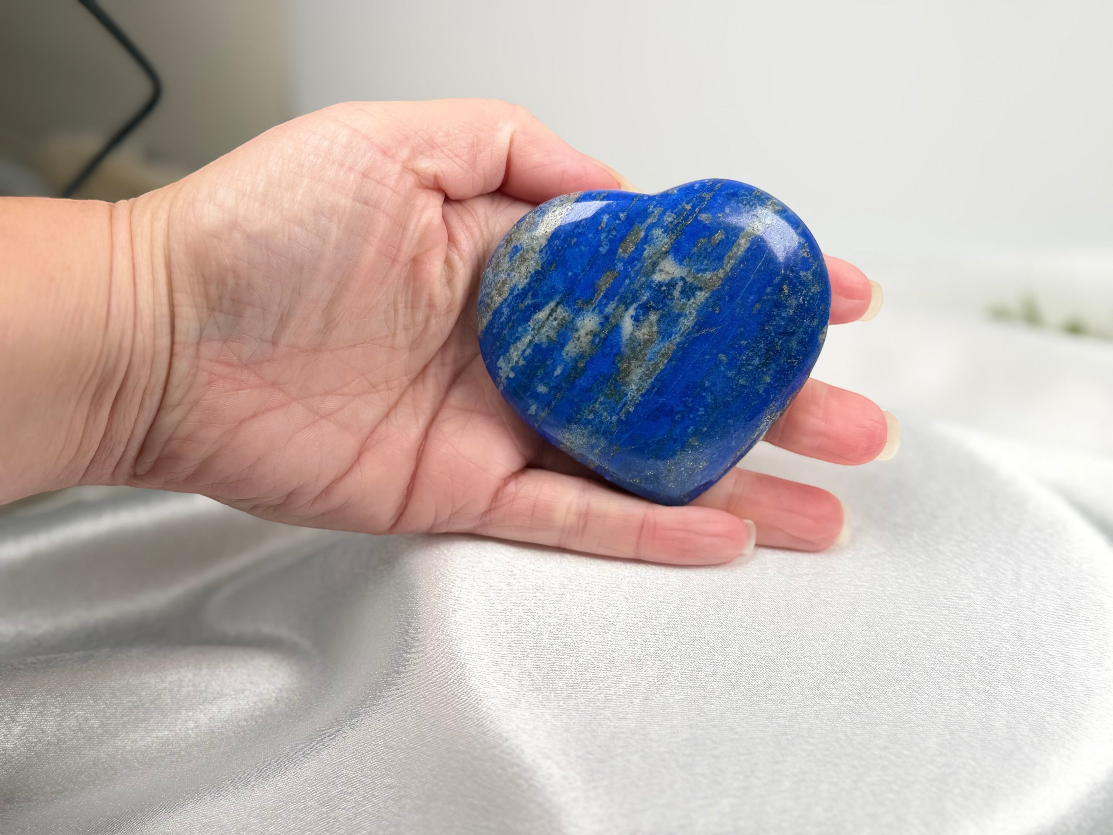 Treasured Energies large polished Lapis Lazuli crystal heart held in a palm, showing deep blue with gold pyrite flecks.