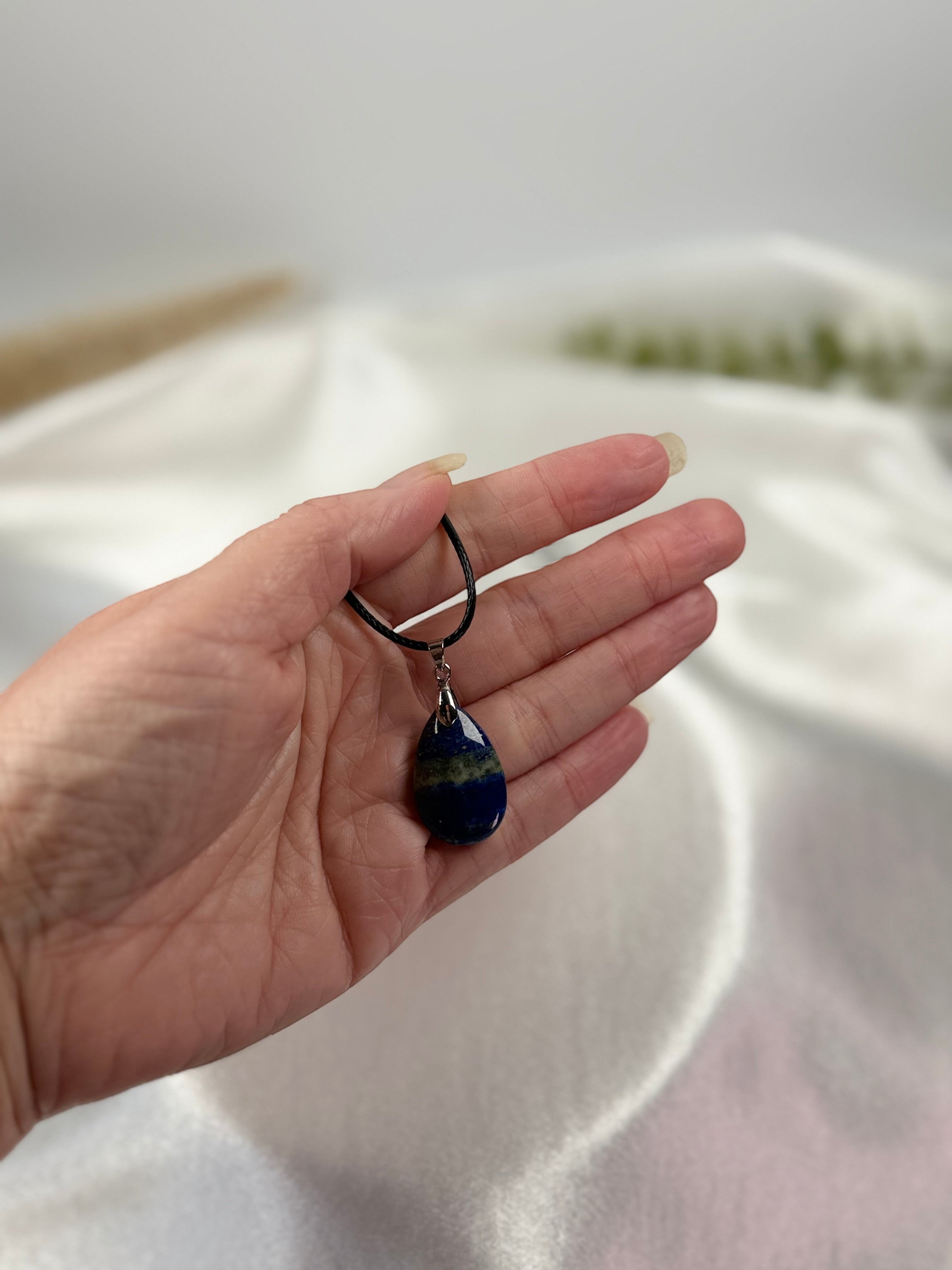 Treasured Energies teardrop Lapis Lazuli pendant necklace with golden pyrite flecks held in a hand.