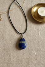 Treasured Energies teardrop Lapis Lazuli pendant on a black cord necklace held in a palm, showing blue stone details.