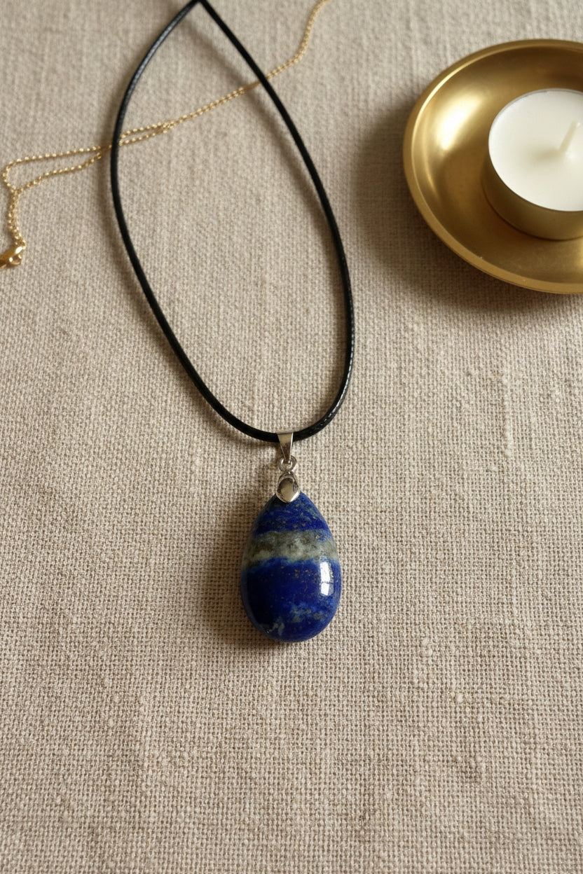 Treasured Energies teardrop Lapis Lazuli pendant on a black cord necklace held in a palm, showing blue stone details.