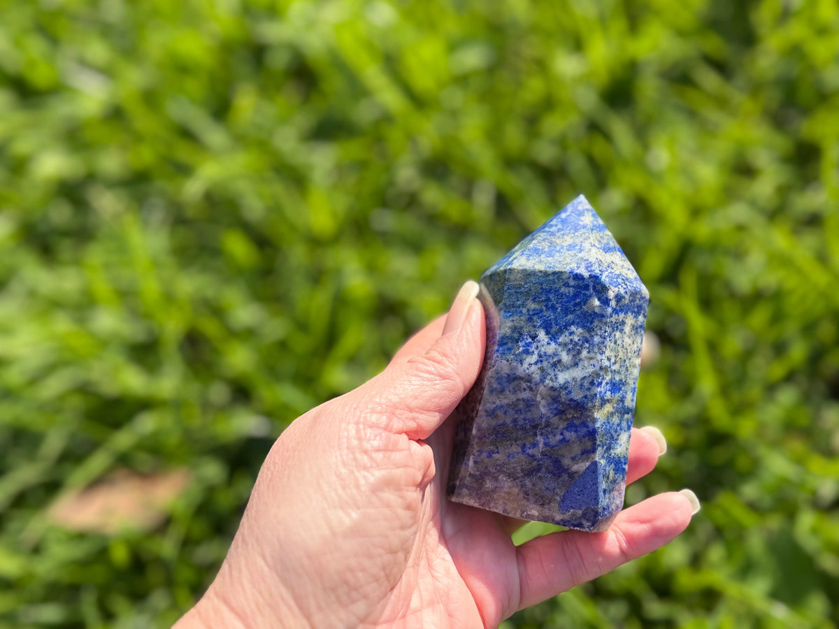 Treasured Energies medium Lapis Lazuli crystal tower held in hand against a blurred green grass background.