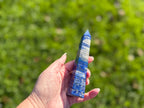 Treasured Energies Lapis Lazuli crystal tower held in hand, featuring deep blue stone with white calcite and gold pyrite.