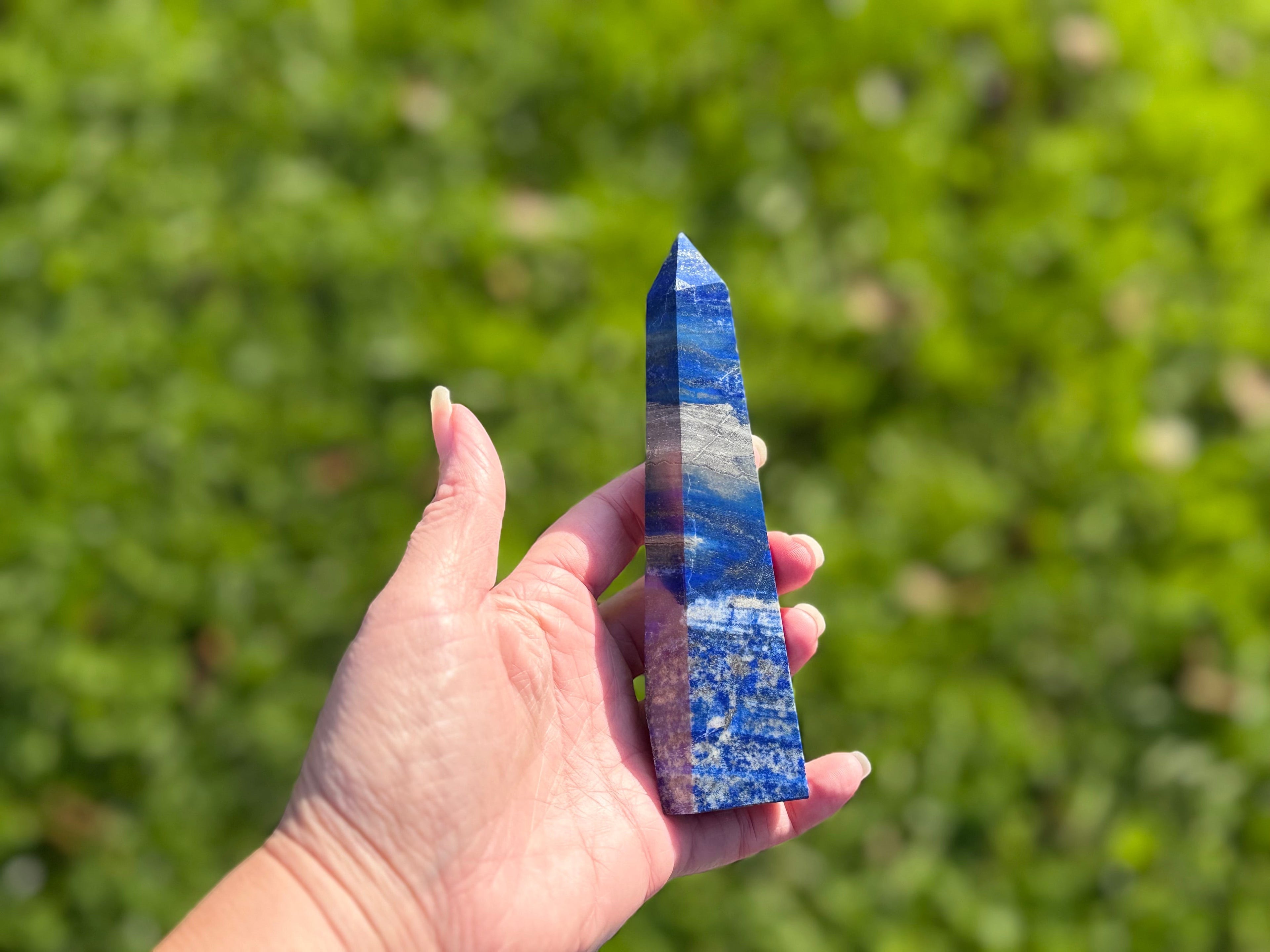 Treasured Energies Lapis Lazuli crystal tower held in hand, showing deep blue stone with golden pyrite and white calcite.