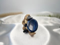 Treasured Energies Lapis Lazuli worry stone held by a small platypus figurine on a white satin fabric background.