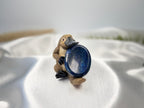 Treasured Energies Lapis Lazuli worry stone held by a small platypus figurine on a white satin fabric background.
