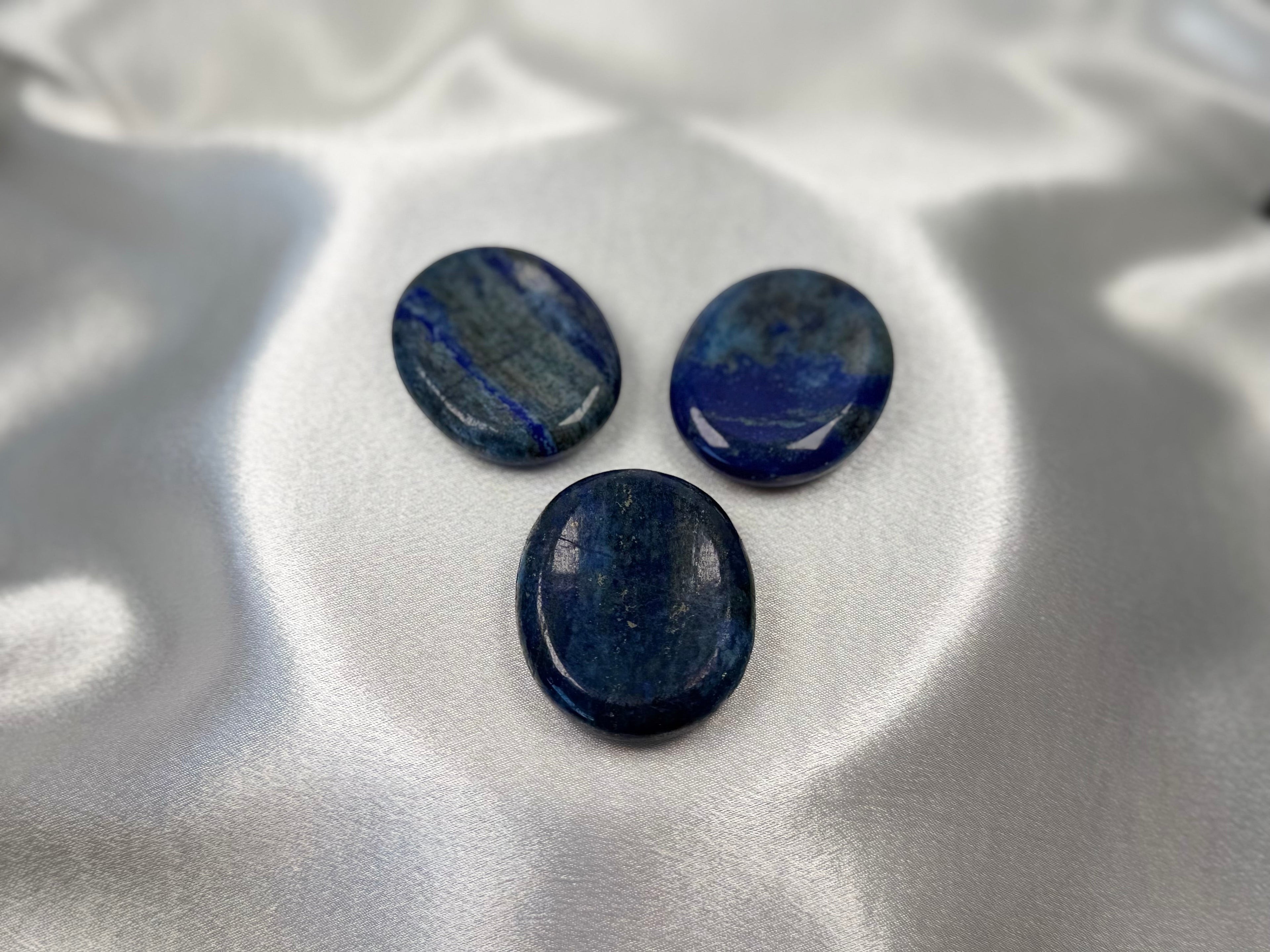 Treasured Energies Lapis Lazuli worry stones with deep blue colour and gold pyrite flecks on a white satin background