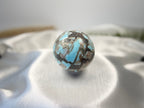 Treasured Energies polished Larimar crystal sphere with blue and brown patterns on a white satin background