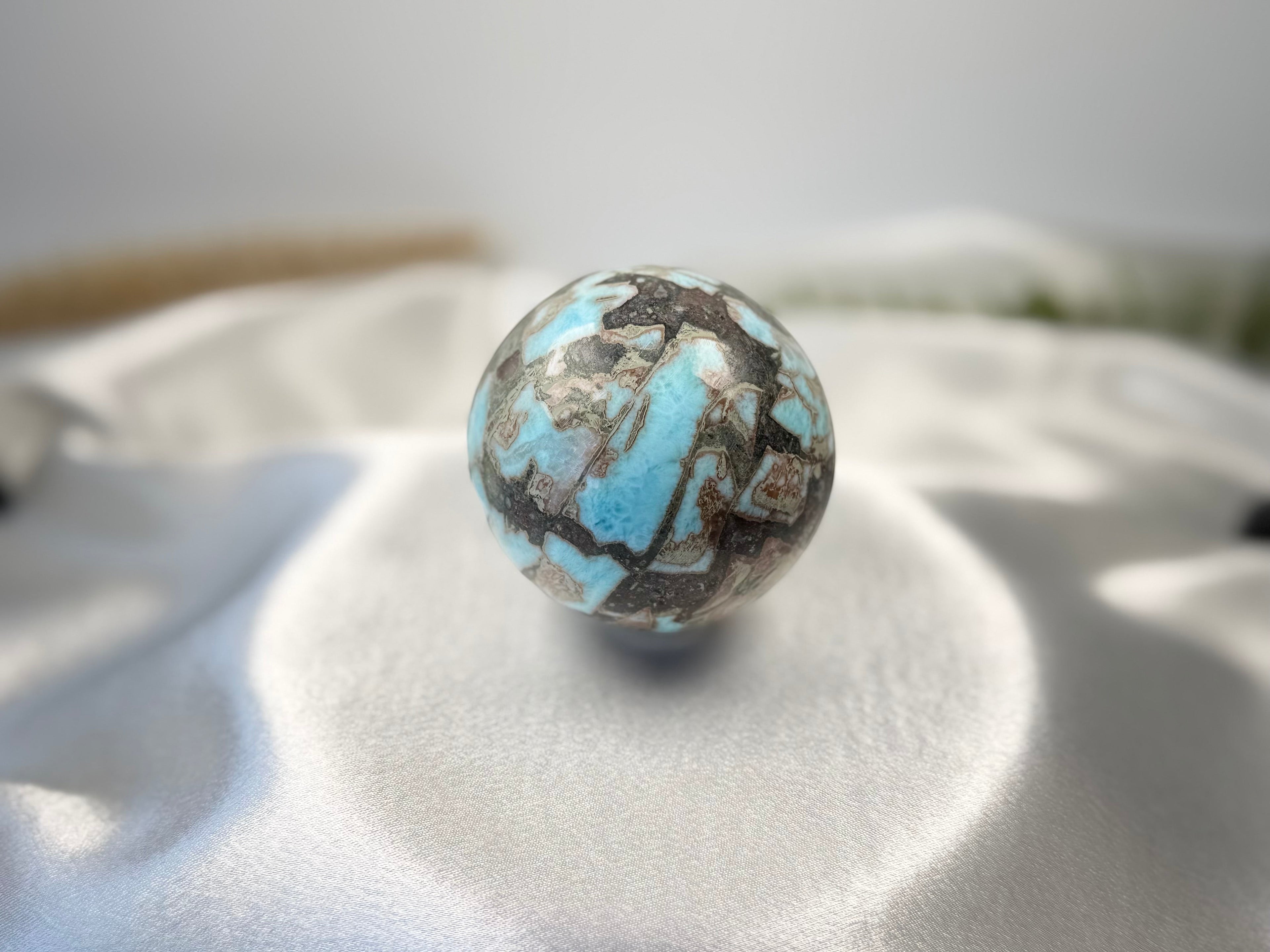 Treasured Energies polished Larimar crystal sphere with blue and brown patterns on a white satin background