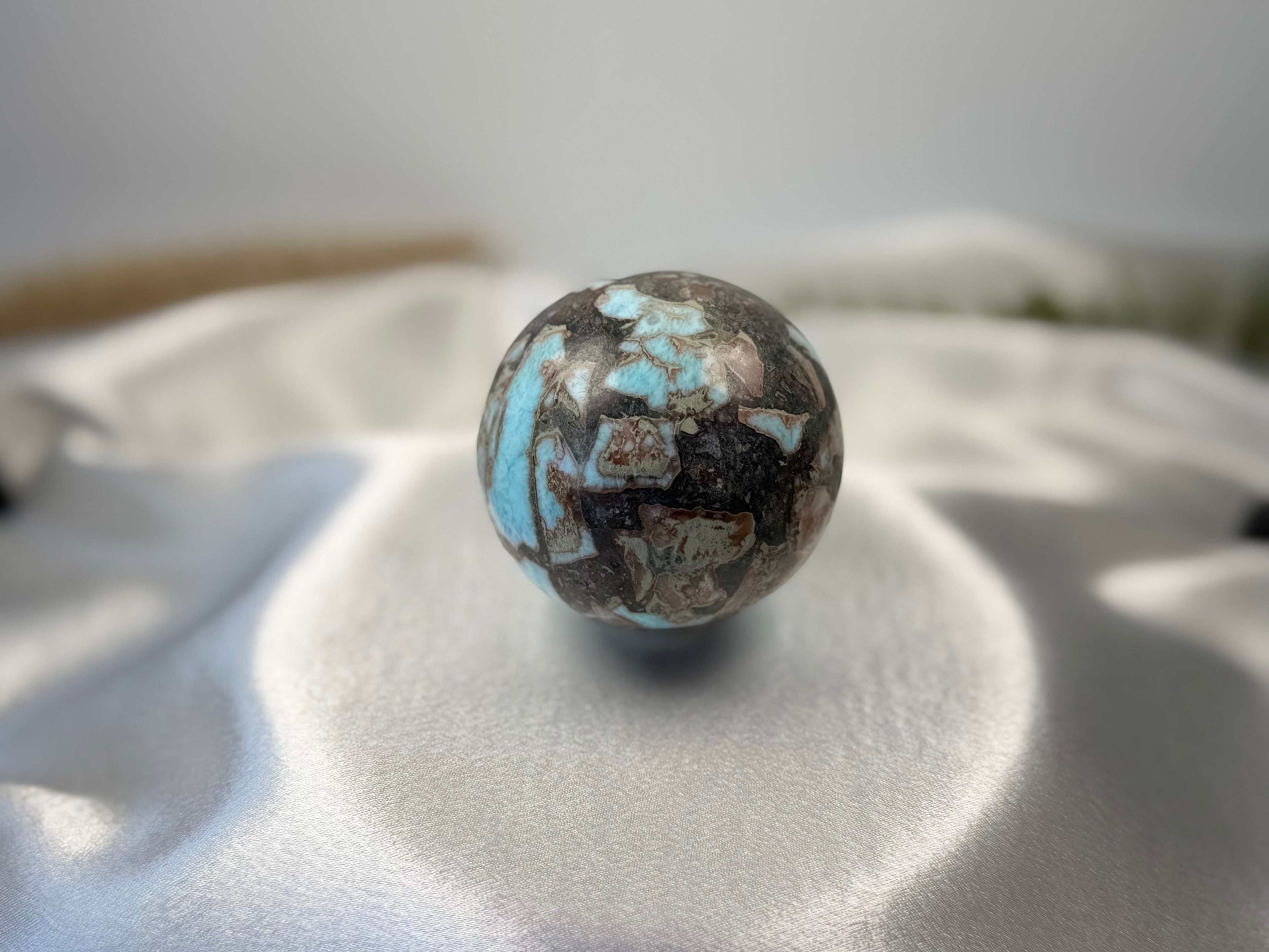 Treasured Energies polished Larimar crystal sphere with blue and dark brown matrix patterns on a white satin cloth.