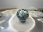 Treasured Energies polished Larimar crystal sphere with blue and brown patterns on a soft white satin fabric background.
