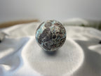 Treasured Energies polished Larimar sphere with blue and dark brown patterns resting on a white satin cloth