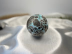 Treasured Energies polished Larimar sphere with blue and dark brown patterns resting on a white satin cloth