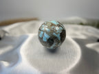 Treasured Energies polished Larimar sphere featuring oceanic blue and grey patterns on a white satin background.