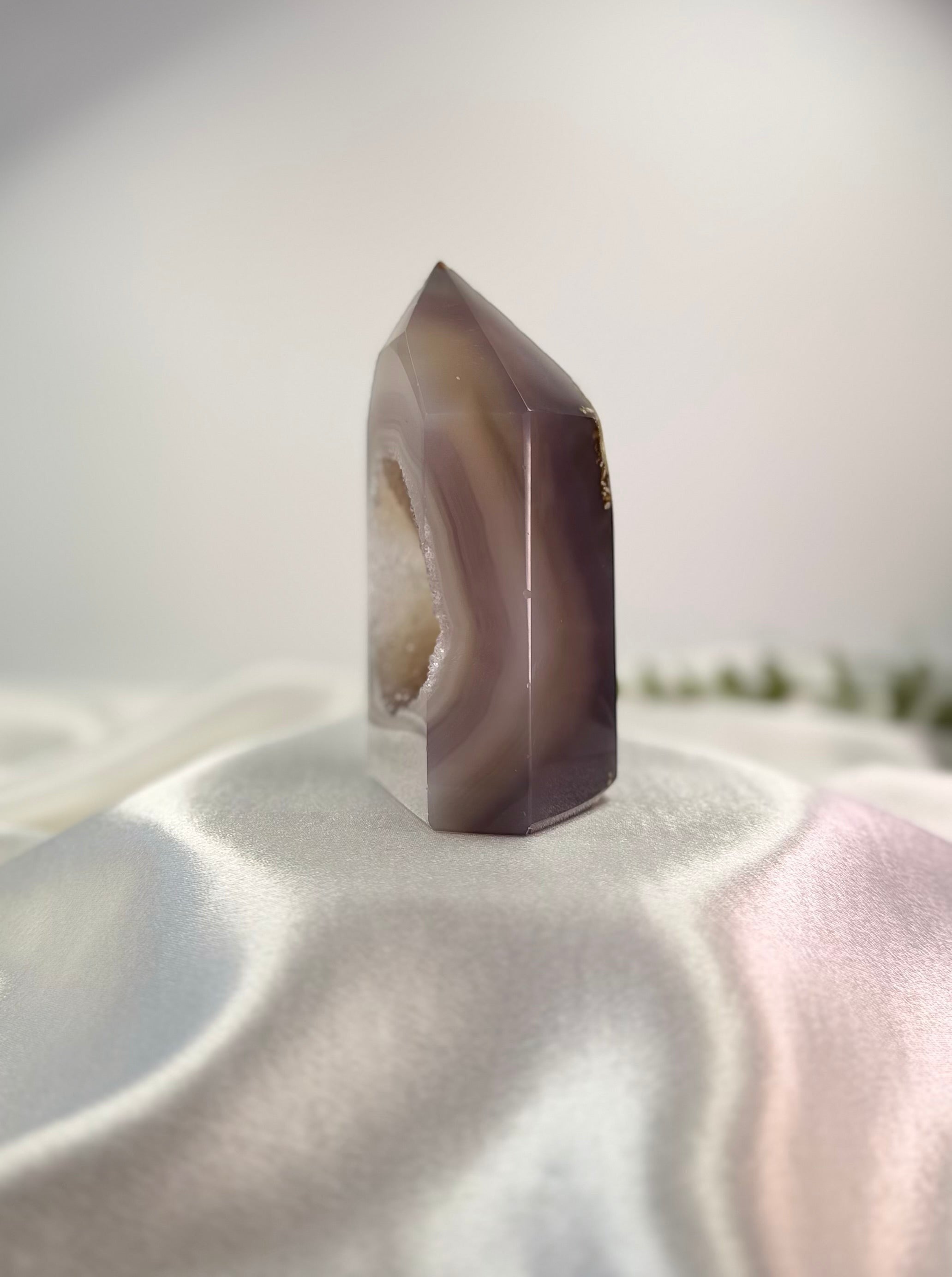 Treasured Energies polished lilac and grey agate crystal tower point with a sparkling druzy interior on satin fabric.