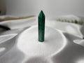 Treasured Energies polished malachite crystal generator tower with signature deep green swirling patterns on white silk