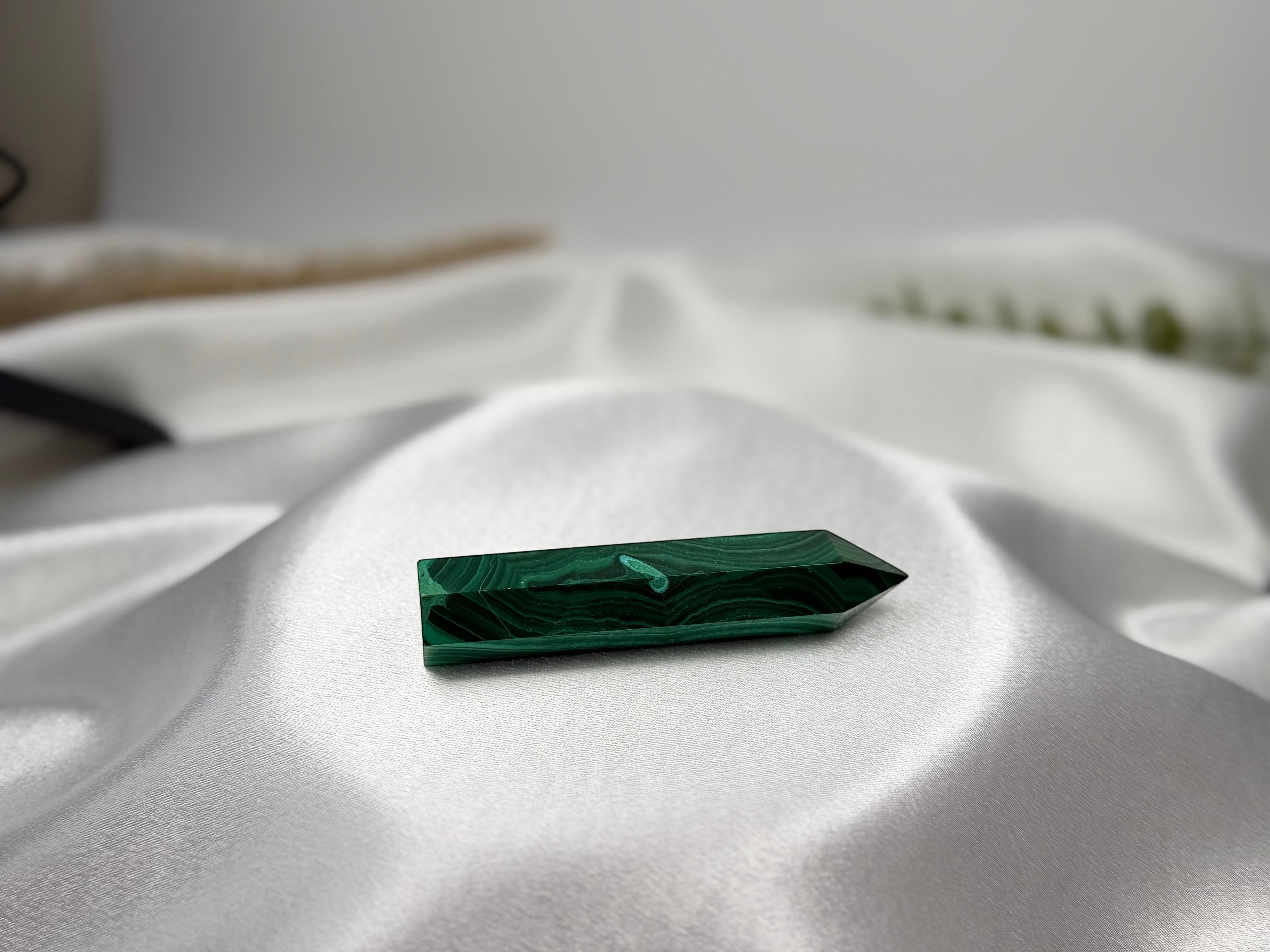 Treasured Energies polished malachite crystal generator tower with deep green banding on a white satin fabric background