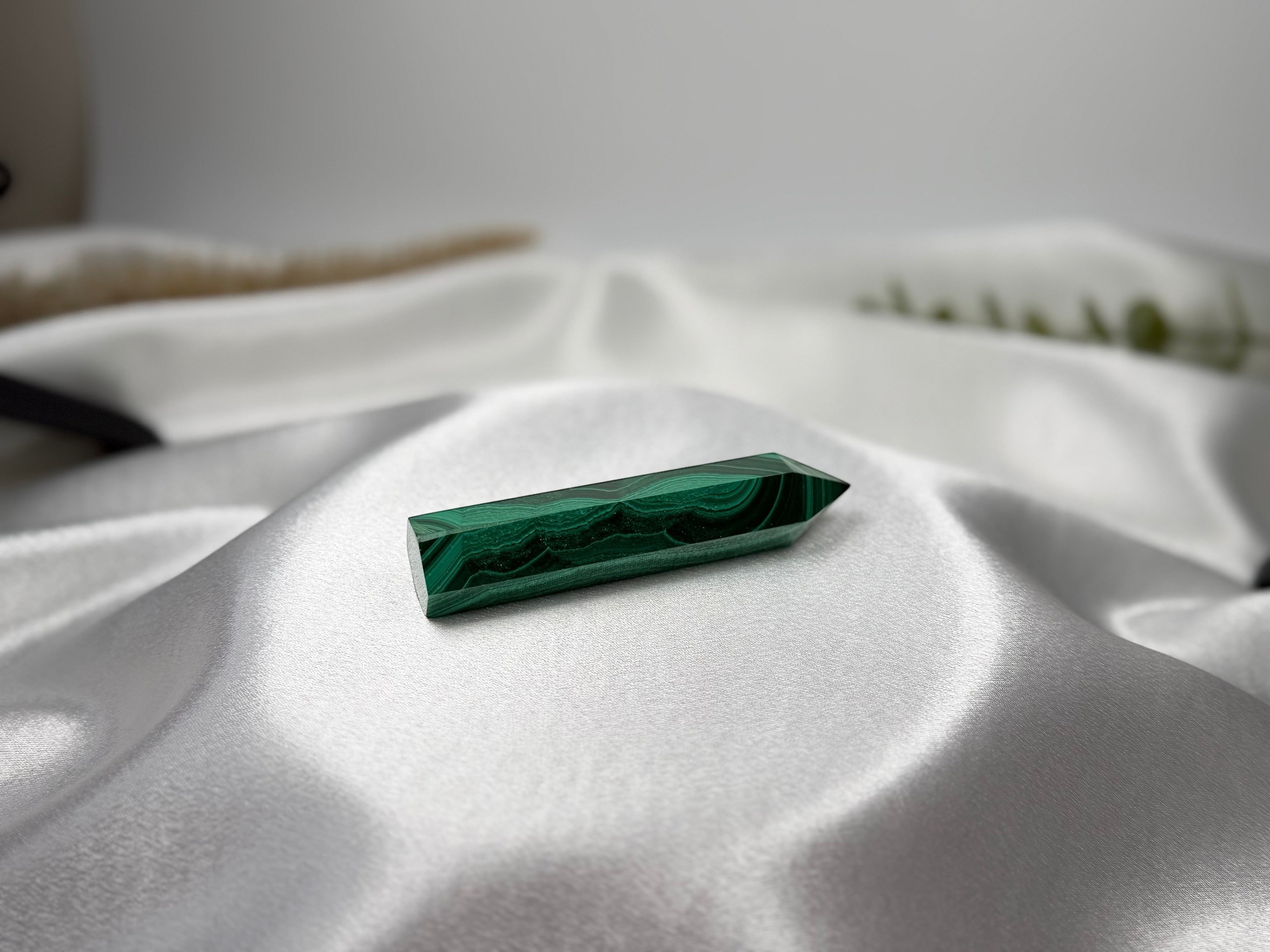 Treasured Energies polished malachite crystal tower with deep green banding resting on white satin fabric.