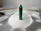 Treasured Energies polished malachite crystal tower with deep green banding on a soft white satin background